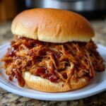 A close-up of a delicious sandwich piled high with saucy slow cooker pulled pork on a soft bun.