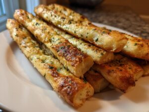 A close-up of a pile of golden, soft breadsticks brushed with garlic butter and sprinkled with parsley.