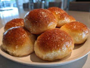 A pile of golden brown, glossy sourdough discard rolls stacked invitingly on a white plate.