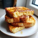 A stack of three thick slices of golden brown easy french toast drizzled with syrup on a white plate.