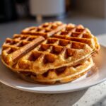 A close-up stack of golden brown, freshly made high protein waffles on a white plate.