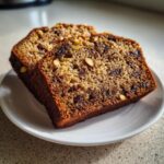 Two thick slices of moist date nut bread, studded with dates and walnuts, resting on a small white plate.