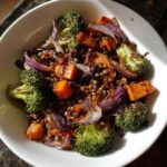 A close-up of a hearty veggie lentil salad featuring roasted broccoli, sweet potato cubes, and red onion mixed with brown lentils.