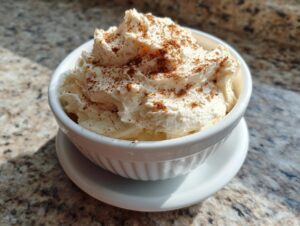 A close-up of fluffy, whipped cinnamon butter generously sprinkled with ground cinnamon, served in a white ramekin.