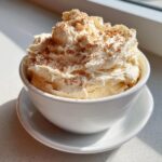 A white bowl filled with creamy, whipped cinnamon butter, generously dusted with ground cinnamon.