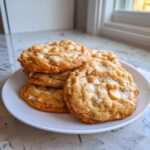 A stack of freshly baked white chocolate macadamia nut cookies piled on a white plate.