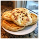A stack of freshly cooked, golden-brown pita bread pockets resting on a white plate.