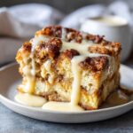 A decadent slice of amazing bread pudding topped with thick vanilla sauce drizzled over the caramelized crust.