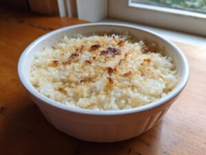 Close-up of baked butter rice with a golden, slightly browned top, served in a white ceramic bowl.