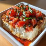 A close-up of a generous serving of baked bruschetta dip, showing the creamy white cheese base topped with fresh diced tomatoes and basil.
