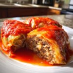 A close-up of three savory cabbage rolls smothered in bright red tomato sauce, one cut open to show the meat and rice filling.