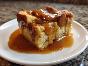 Close-up of a square slice of bread pudding with bourbon sauce generously drizzled over the top.