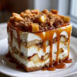 A tall, layered slice of caramel apple trifle featuring cream, graham cracker layers, apples, and heavy caramel sauce dripping down the sides.