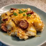 A close-up serving of pierogi casserole topped with melted cheddar cheese, sliced sausage, and green onions.