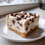 A single, perfect square slice of creamy chocolate chip cheesecake resting on a white plate.
