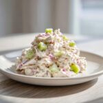 A mound of creamy cottage cheese chicken salad mixed with chunks of cucumber and red onion served on a white plate.