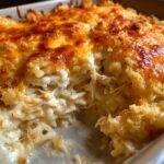 Close-up of a creamy chicken and rice casserole with a bubbly, golden-brown cheese and breadcrumb topping.