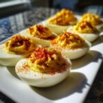 A plate of perfectly piped classic deviled eggs sprinkled generously with bright red paprika.
