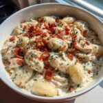 Close-up of a white bowl filled with creamy crack chicken gnocchi, topped generously with bacon bits and herbs.