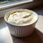 A small white ramekin filled with thick, creamy homemade garlic sauce, topped with black pepper.