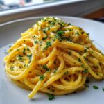 A close-up shot of a mound of creamy lemon pasta tossed in a bright yellow sauce and topped with fresh chopped parsley.