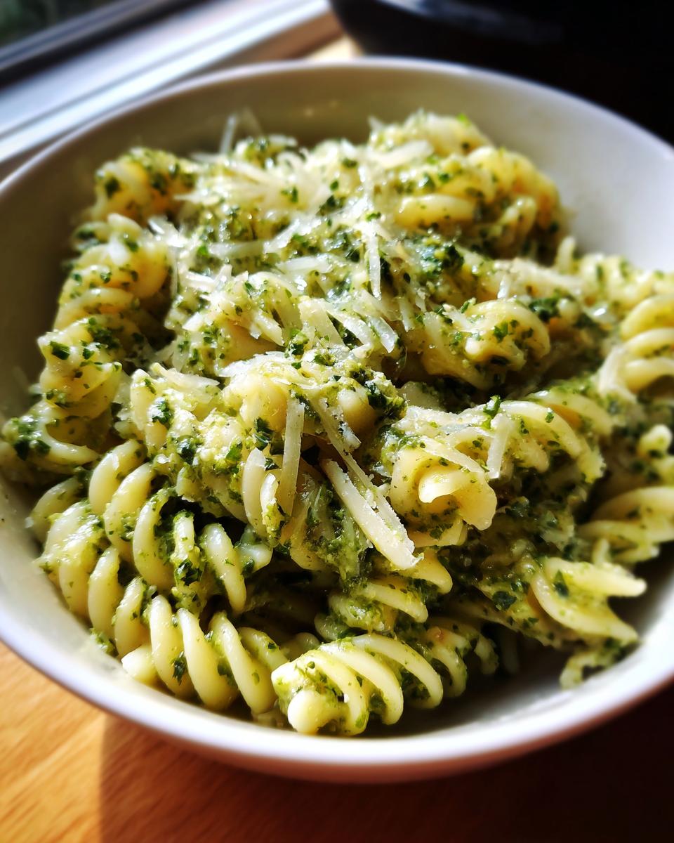 Close-up of creamy pesto pasta made with fusilli noodles, generously topped with shredded Parmesan cheese.