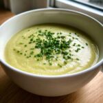 A close-up of creamy potato leek soup in a white bowl, garnished generously with freshly chopped green chives.