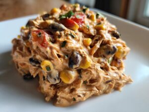 A close-up of creamy, shredded southwest chicken salad mixed with black beans, corn, and tomatoes, served on a white plate.
