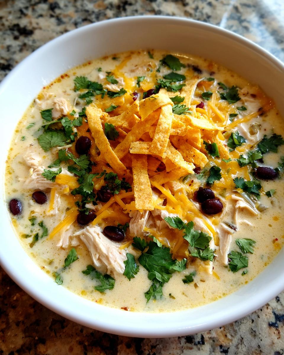 Close-up of a bowl of creamy tortilla soup with shredded chicken, black beans, cheese, and crispy tortilla strips.