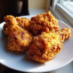 Four pieces of golden brown, crispy air fryer fried chicken served on a white plate near a window.