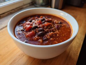 A close-up of a white bowl filled with steaming, rich black bean chili featuring visible beans and tomatoes.
