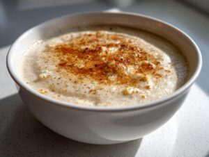 Close-up of a white bowl filled with creamy roasted cauliflower soup, topped with a dusting of paprika or nutmeg.