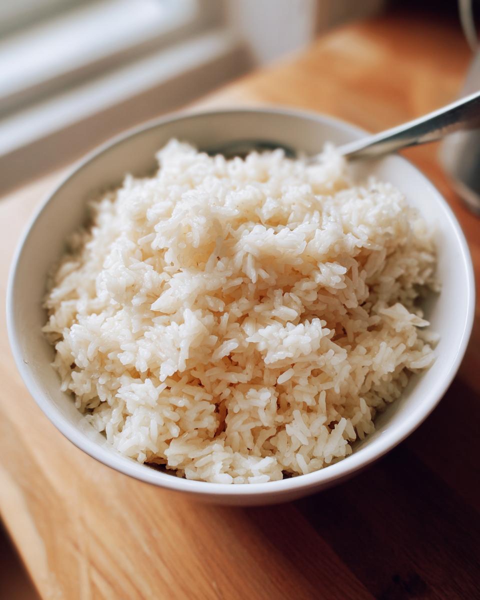 Close-up of a white bowl filled with fluffy, perfectly cooked butter rice, resting on a wooden surface.