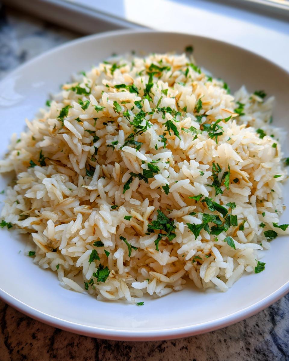 Close-up of a white bowl filled with fluffy rice pilaf, featuring toasted vermicelli and fresh chopped parsley garnish.