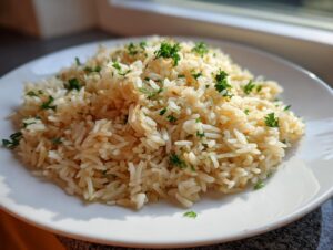 A mound of fluffy, perfectly cooked rice pilaf garnished with chopped green parsley on a white plate.