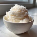 A close-up of fluffy, white snow ice cream topped with fine shavings in a small white bowl.