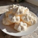 A mound of light, fluffy whipped shortbread cookies piped into star shapes, resting on a white plate.