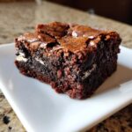 A close-up of a fudgy square of Oreo brownies showing the shiny, crackly top and white cream filling.