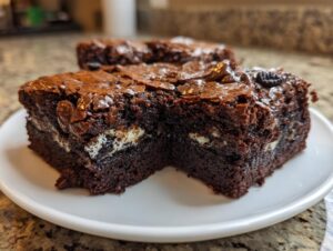 Two fudgy Oreo brownies cut in half, showing creamy white filling and a shiny, crackly top.