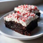 Two slices of fudgy peppermint brownies topped with thick white frosting and crushed candy canes.
