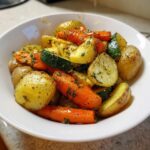 A white bowl filled with vibrant Garlic Herb Roasted Veggies, including potatoes, carrots, and zucchini, seasoned with herbs.