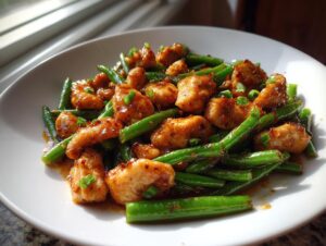 A close-up of glazed chicken and green beans stir-fry served on a white plate, garnished with green onions.