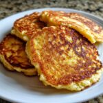 Close-up of four perfectly golden brown coconut flour pancakes stacked slightly on a white plate.