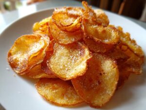 Close-up of a pile of golden, crispy homemade potato chips seasoned with visible salt crystals.