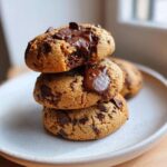 Three delicious vegan chocolate chip cookies stacked with melted chocolate oozing out.