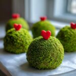 Close-up of several green grinch oreo balls coated in green crumbs and topped with a small red heart candy.
