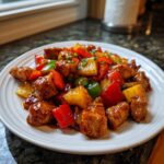 Close-up of glazed hawaiian chicken sheet pan pieces mixed with pineapple and bell peppers on a white plate.