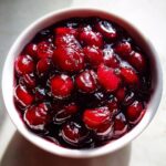 Overhead close-up of vibrant, glossy cherry pie filling with whole cherries in a white bowl.