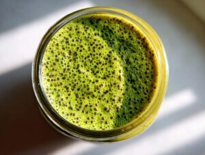 Overhead view of bright green matcha chia pudding topped with visible chia seeds in a glass jar.