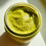 Overhead close-up of vibrant green matcha chia pudding speckled with dark chia seeds in a glass jar.